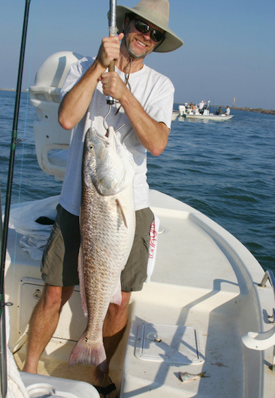 Fisherman holds big redfish while standing in boat.