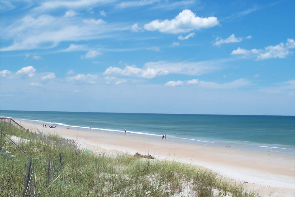 Sunny day at the beach with sand dunes in the foreground.